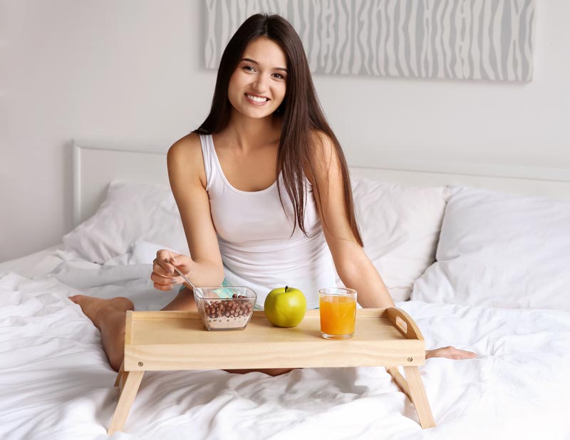 Young woman smiling while having breakfast at bed